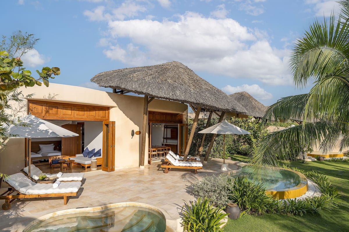 A resort with outdoor seating, a pool, and thatched-roof structures.
