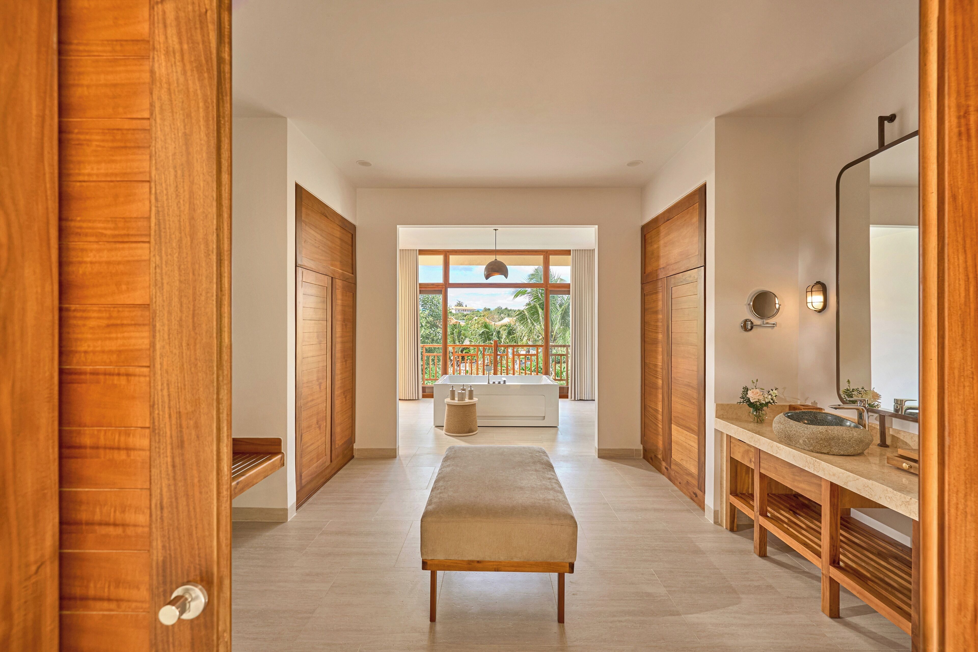 A hallway leading to a bathroom with a bathtub, wooden flooring, and a bench.