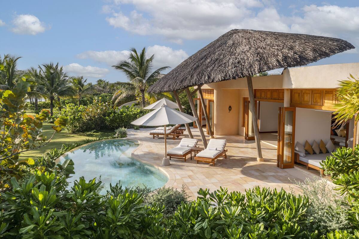 A poolside area with lounge chairs, a thatched umbrella, and a pool.