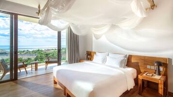 Ein geräumiges Schlafzimmer mit einem großen Bett, einem Holz-Kopfschild und einem Nachttisch mit Lampe. Ein Balkon mit Meerblick ist sichtbar.