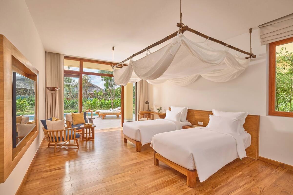 A room with two beds, a wooden floor, a large window, and a view of greenery outside.