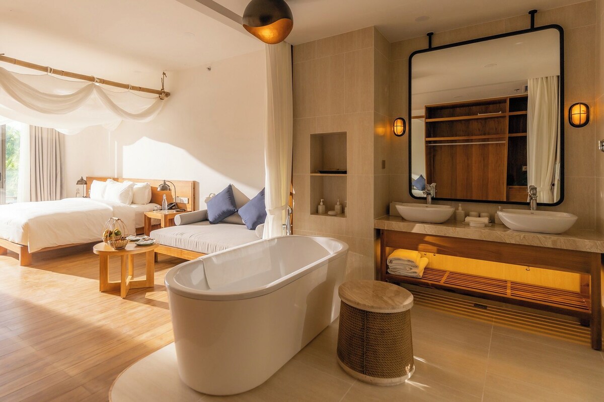 Une chambre d’hôtel moderne dotée d’un grand lit, d’un coin salon, d’une baignoire et d’une salle de bain avec un grand miroir et un lavabo.
