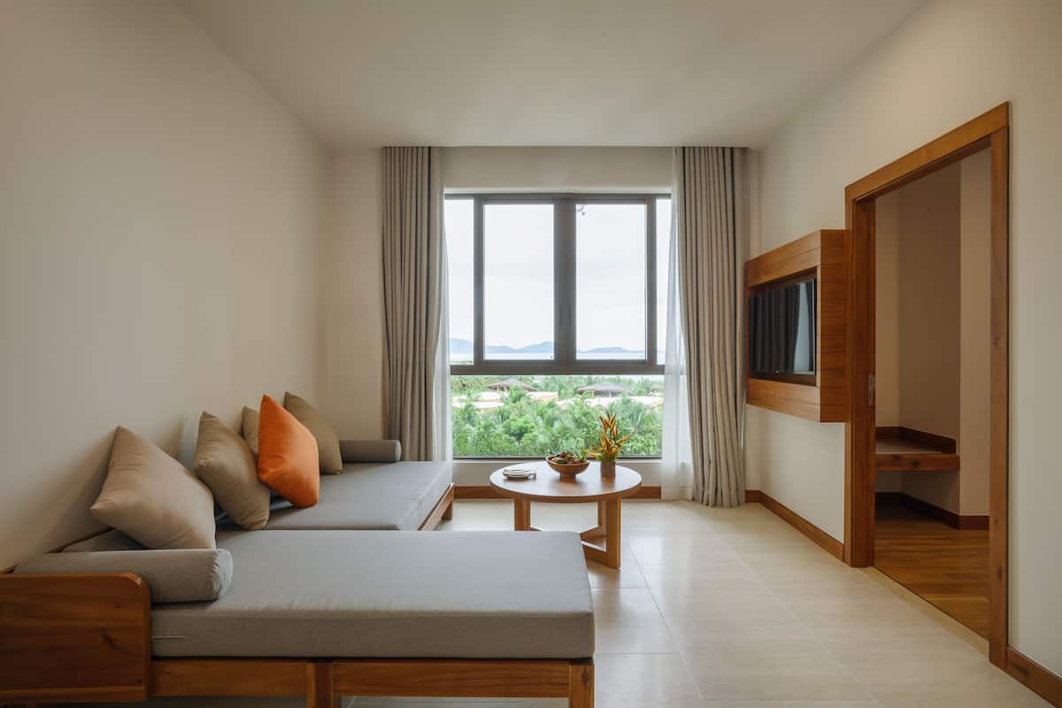 A modern living room with a sofa, a small round table with a plant, and a large window offering a view of greenery.