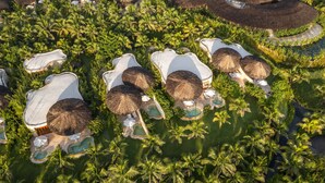 An aerial view of a resort with multiple thatched-roof huts, swimming pools, and lush palm trees. - Ana Mandara Cam Ranh (Cam Lam)
