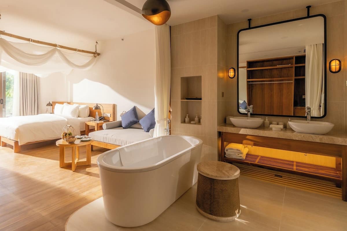Une chambre d’hôtel moderne dotée d’un grand lit, d’un coin salon, d’une baignoire et d’une salle de bain avec un grand miroir et un lavabo.