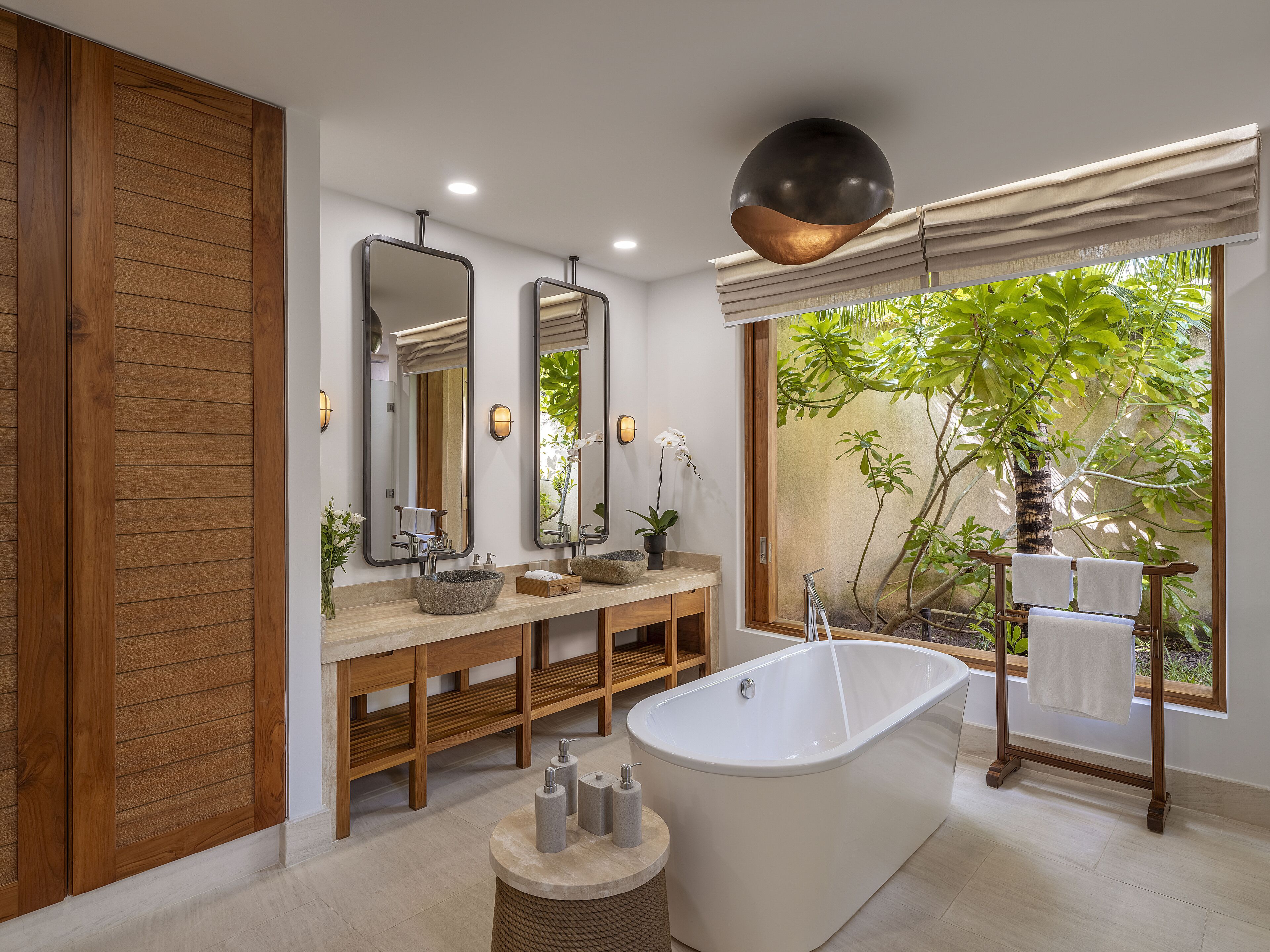 Un baño moderno con una bañera independiente, tocador de madera y espejos grandes.