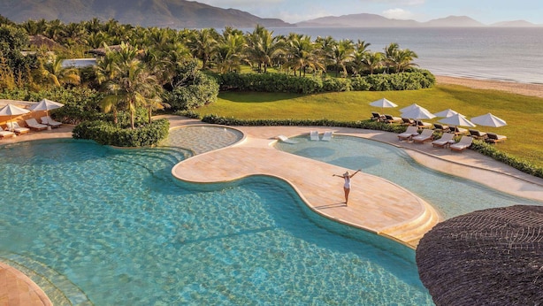 A resort with a large pool, lounge chairs, umbrellas, and a view of the ocean and mountains. - Ana Mandara Cam Ranh (Cam Lam)