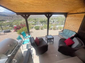 Un patio exterior con una parrilla, mobiliario de mimbre y vistas a un paisaje desértico.