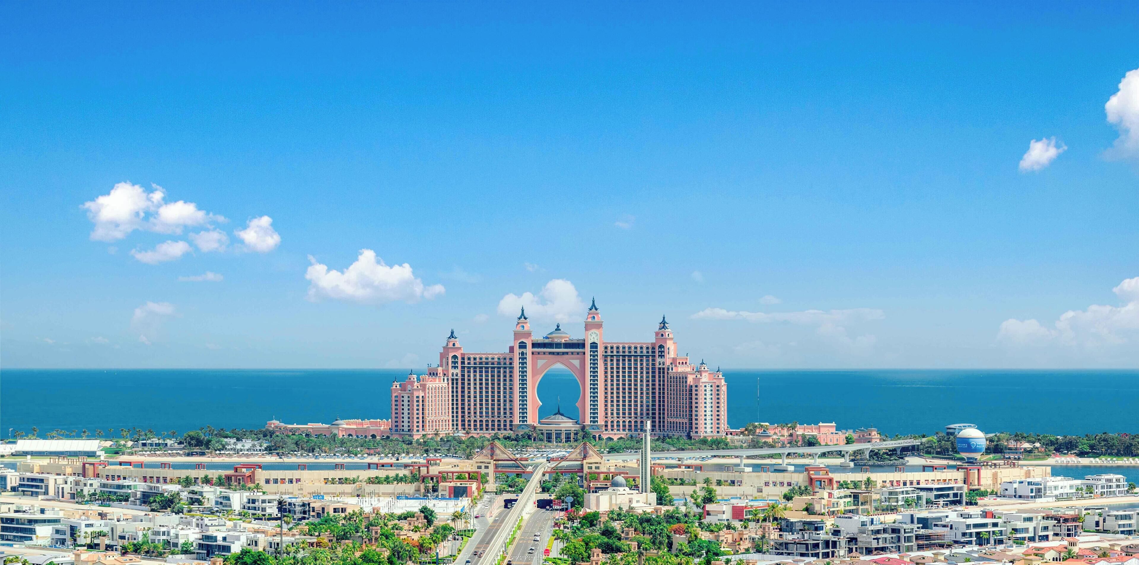 A large hotel with a distinctive arch entrance, multiple towers, and a view of the ocean.