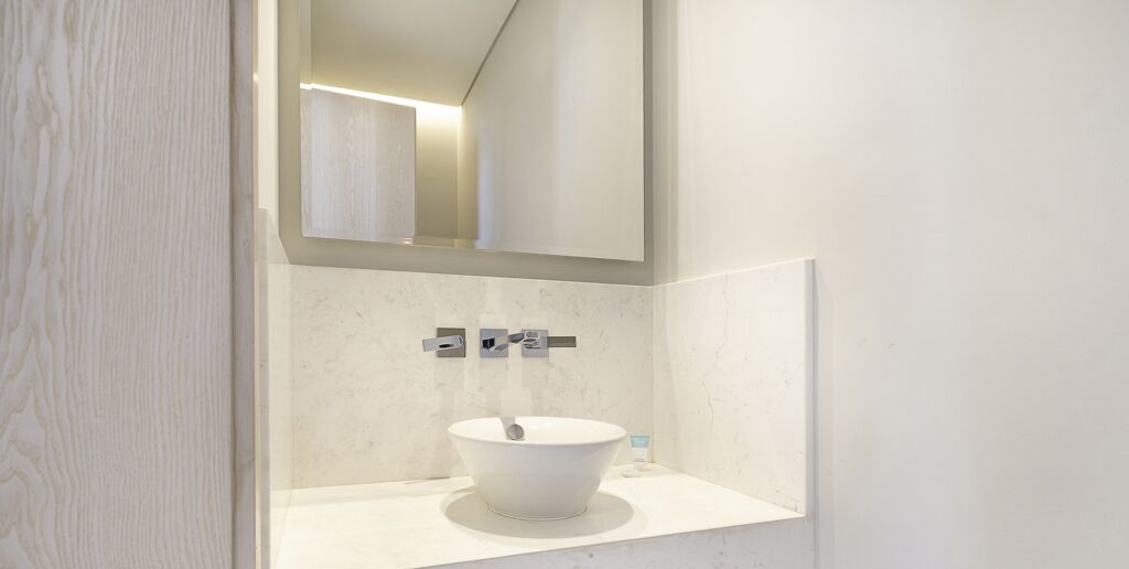 A modern bathroom with a white sink, a mirror, and a small bottle of hand soap on the counter.