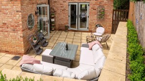 A patio with a white sofa, a table, and chairs, a brick wall, and a wooden fence. - Orchard Cottage, Alderton - sleeps 6 guests  in 3 bedrooms (Alderton)