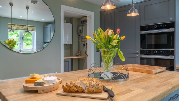 A kitchen with a wooden countertop, a mirror, a vase with flowers, and a clock. - Orchard Cottage, Alderton - sleeps 6 guests  in 3 bedrooms (Alderton)