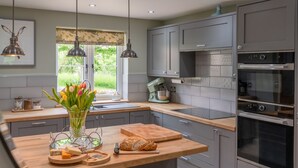 A modern kitchen with grey cabinetry, a built-in oven, and a window with a view of greenery. - Orchard Cottage, Alderton - sleeps 6 guests  in 3 bedrooms (Alderton)