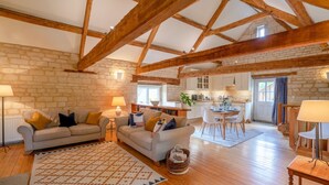 A spacious living area with exposed wooden beams, a stone wall, and a cozy seating arrangement. - Stable Cottage at Freams Farm, Painswick - sleeps 5 guests  in 3 bedrooms (Painswick)
