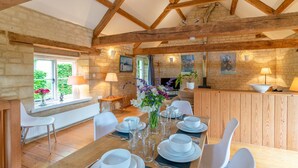 A dining area with a wooden table set for four, surrounded by stone walls and wooden beams. - Stable Cottage at Freams Farm, Painswick - sleeps 5 guests  in 3 bedrooms (Painswick)