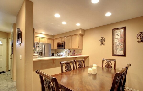 Enjoy meals in this cozy dining area with a wooden table and six chairs, adjacent to a fully equipped kitchen with a refrigerator.