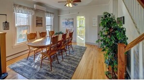 Un coin repas avec une table et des chaises en bois, un ventilateur de plafond et un escalier doté d’une rampe en bois.