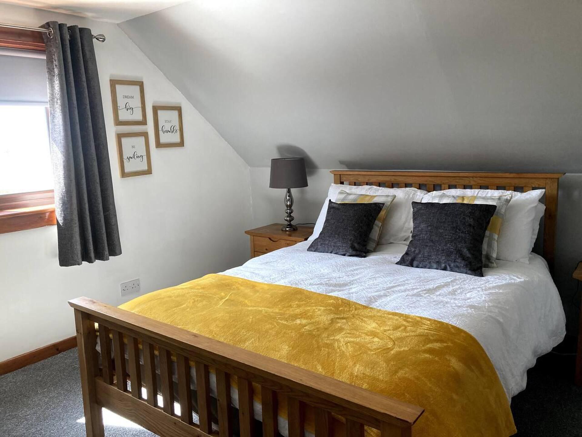 A bedroom with a wooden bed, a nightstand, a lamp, and a window with curtains.