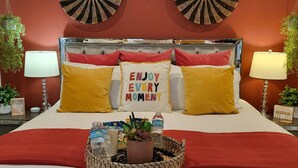 A neatly made bed with a red blanket, two round wall decorations, and a pillow with the text "ENJOY EVERY MOMENT". - Modern Bohemian Studio - in Golf neighborhood - Disney 15 min (Davenport)