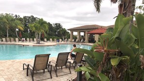 A pool area with lounge chairs, a covered seating area, and a building with a tiled roof.