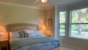 A bedroom with a large bed, two bedside tables, a ceiling fan, and a window with blinds.