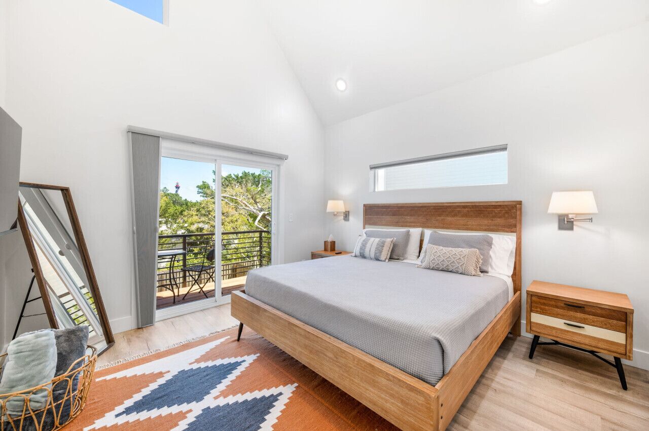 Un dormitorio moderno con una cama grande, un balcón con mobiliario exterior y vistas a zonas verdes.
