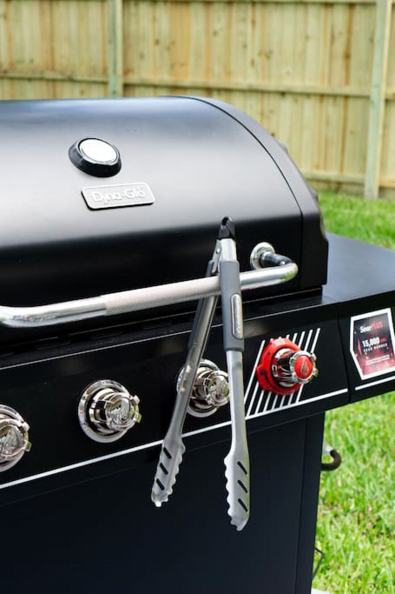 Una parrilla para barbacoa con pantalla digital, perillas de control y unas pinzas.