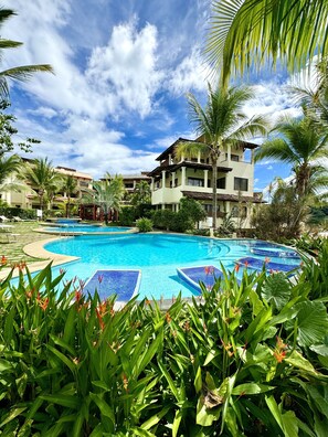 Un complexe hôtelier doté d’une grande piscine, entourée d’une végétation luxuriante et de palmiers.