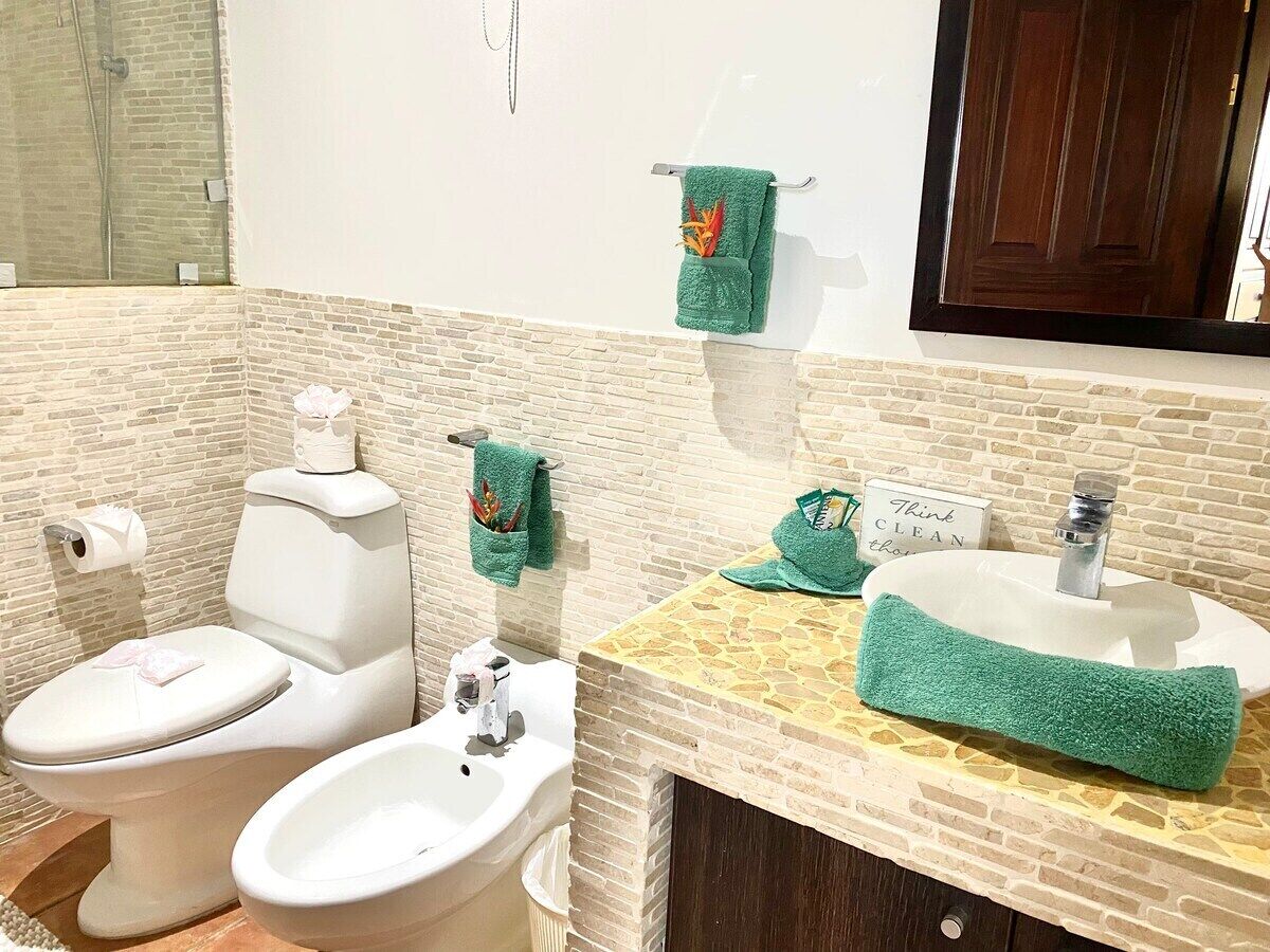 A bathroom with a toilet, bidet, and sink. There are green towels hanging on the wall and a sign that says "Think CLEAN."