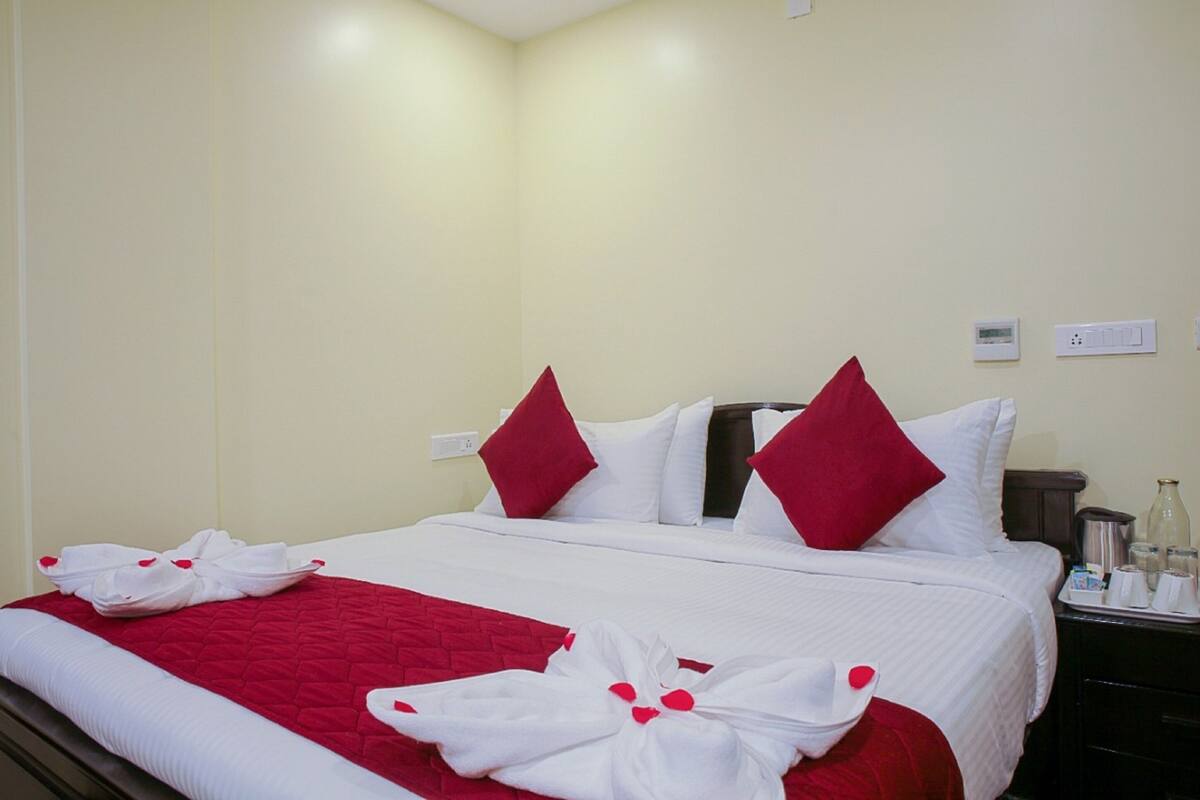 A hotel room with a neatly made bed, red and white bedding, and a red throw blanket.