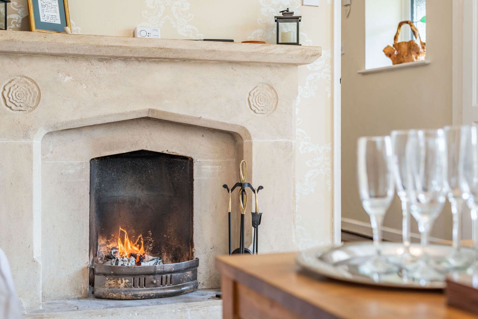 A fireplace with a fire, a mantel with decorative items, and a tray with glasses.