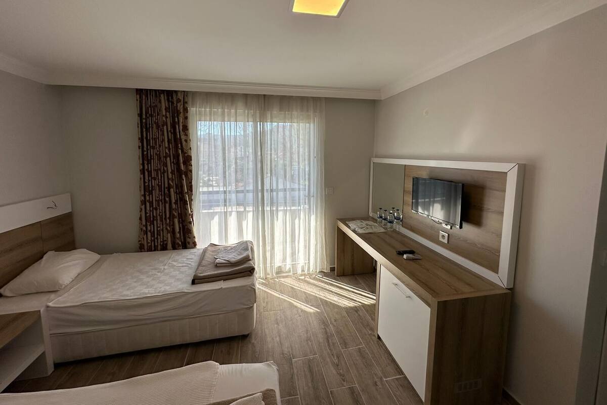 Ein Hotelzimmer mit einem Bett, einem Schreibtisch mit Fernseher und einem Fenster mit Vorhängen.