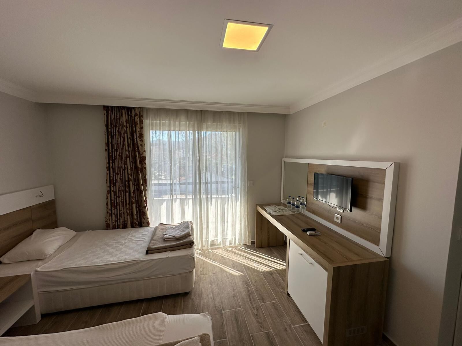 A hotel room with a bed, a desk with a TV, and a window with curtains.