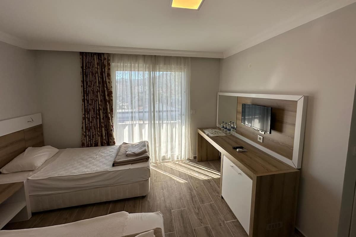 Ein Hotelzimmer mit einem Bett, einem Schreibtisch mit Fernseher und einem Fenster mit Vorhängen.