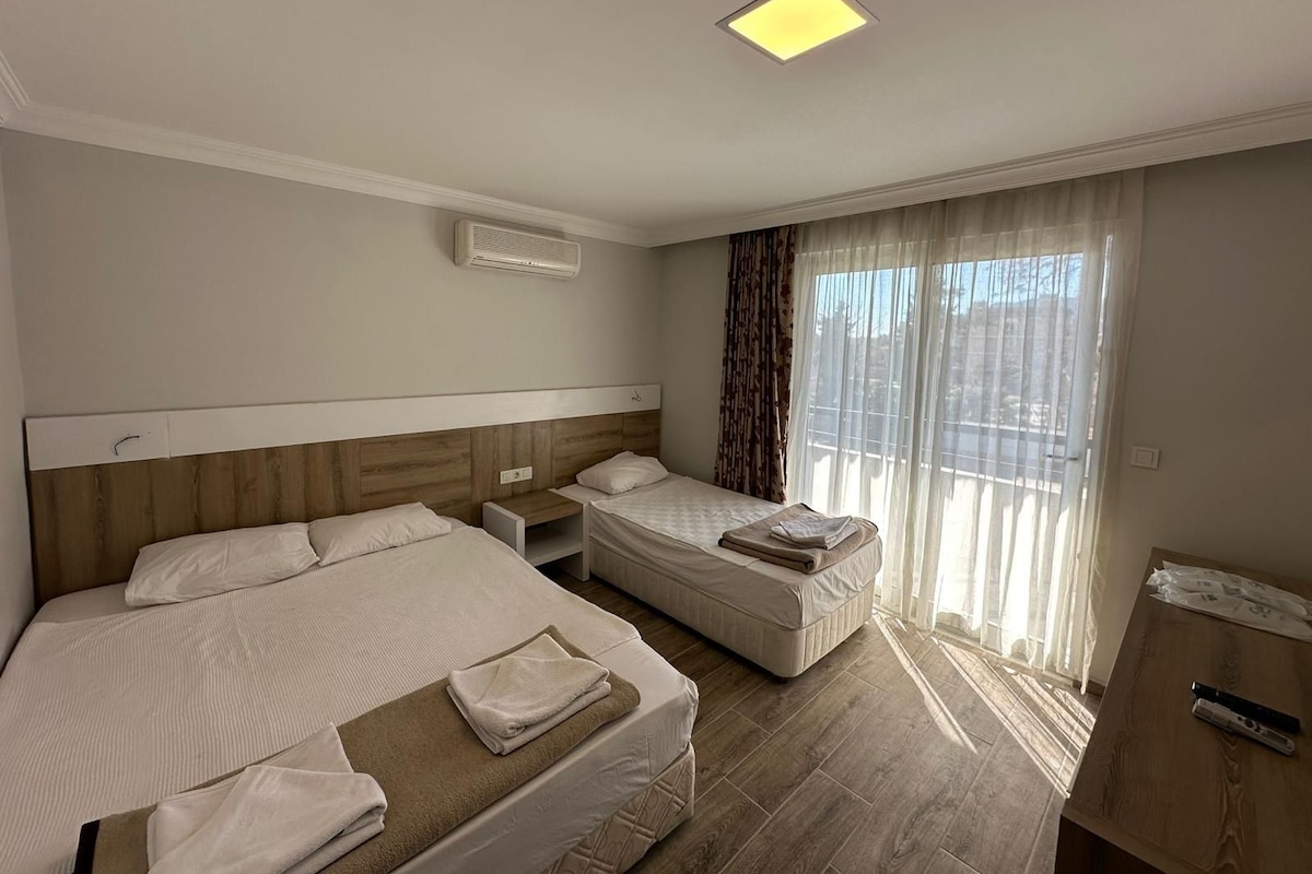 A hotel room with two beds, a bedside table, a desk, and a window with curtains.