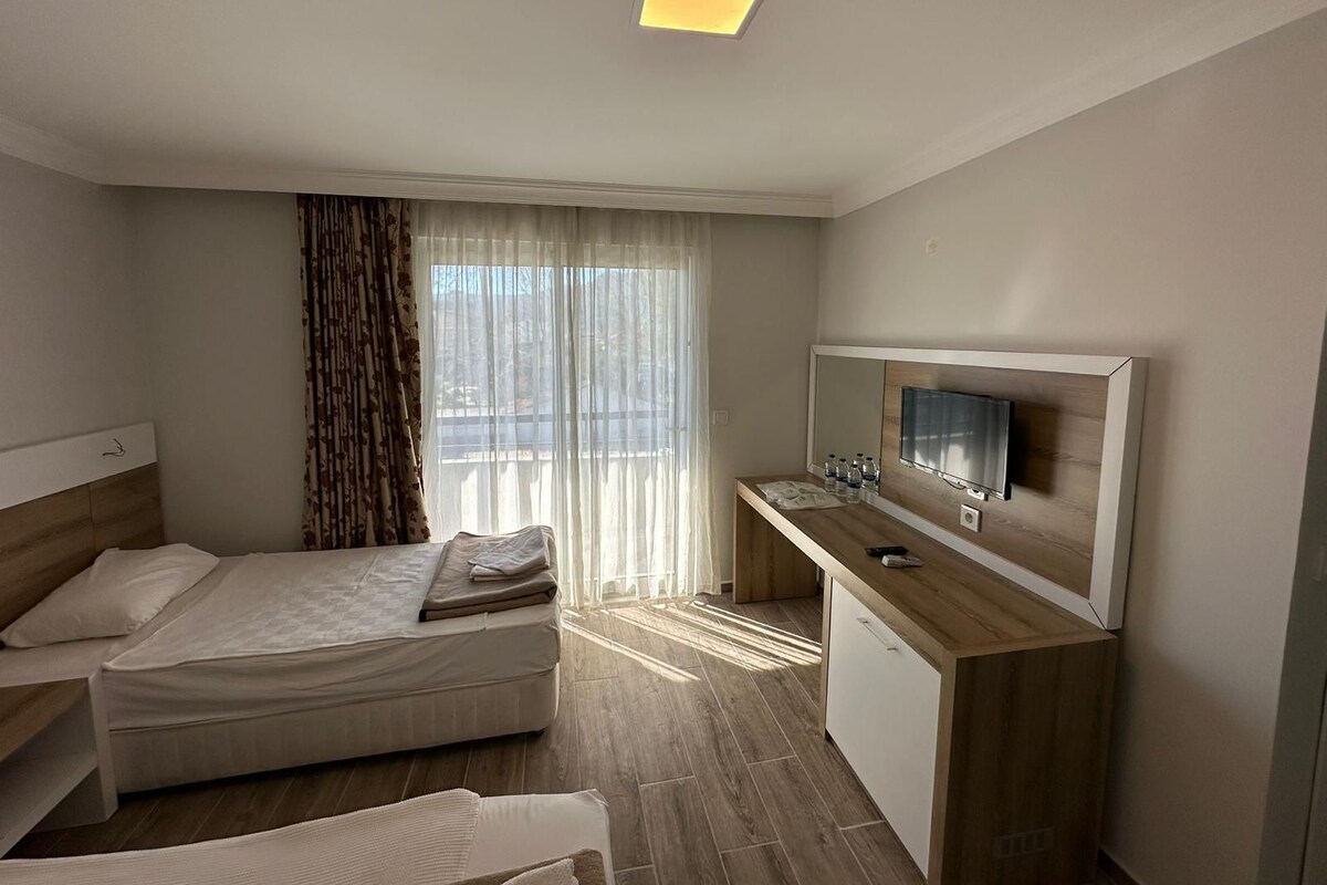 A hotel room with a bed, a desk with a TV, and a window with curtains.