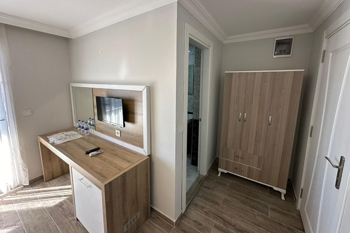 Una habitación con un escritorio de madera, un televisor montado en la pared, un armario y una puerta que da a otra habitación.