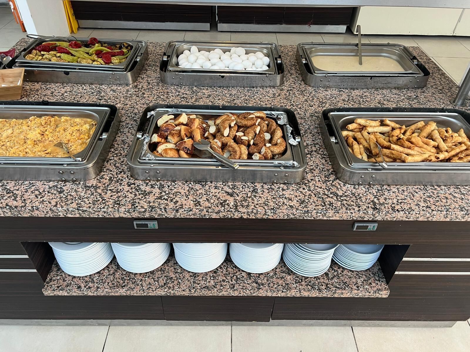 Buffet com diversos alimentos dispostos em bandejas, incluindo ovos, legumes e doces.