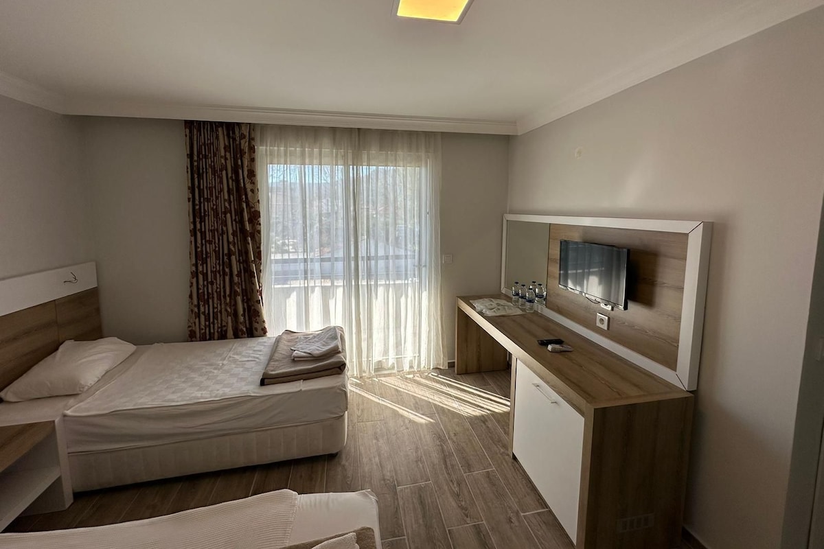 A hotel room with a bed, a desk with a TV, and a window with curtains.