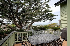 Een balkon met een metalen tafel en stoelen, een grote boom en uitzicht op de oceaan.