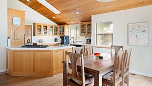 A kitchen with wooden cabinets, a central island, and a dining area with wooden chairs. - Casa Orlando Marine Terrace (Cambria)
