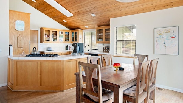 A kitchen with wooden cabinets, a central island, and a dining area with wooden chairs.