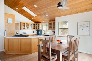 A kitchen with wooden cabinets, a central island, and a dining area with wooden chairs. - Casa Orlando Marine Terrace (Cambria)