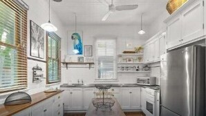 A kitchen with white cabinets, a stainless steel refrigerator, wooden countertops, and a dining table. - Massinger Hideaway (Byron Shire)