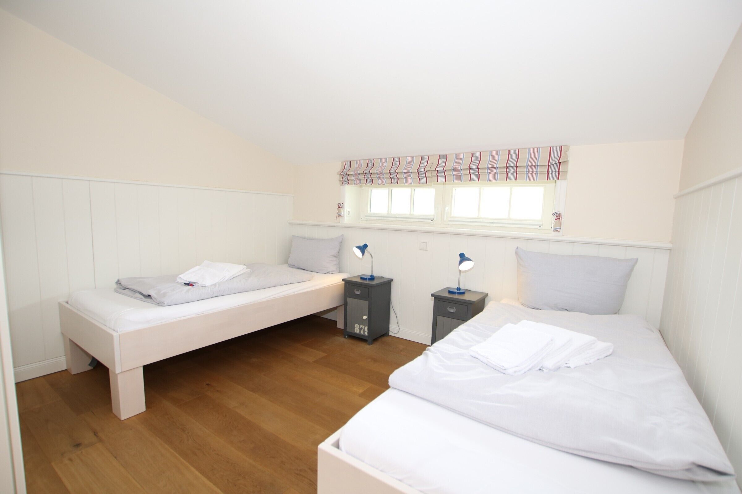 A bedroom with two single beds, a window with a striped valance, and bedside tables with lamps.