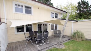 Eine überdachte Terrasse mit Gartenmöbeln, ein Holzboden und ein Haus mit beiger Fassade.