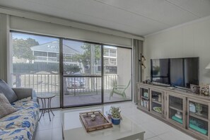 Ein Wohnzimmer mit einer Couch, einem Couchtisch, einem Fernseher und einer Schiebetür zu einem Balkon.