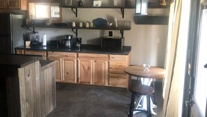 Una cocina con armarios de madera, encimera negra, cafetera y lámpara colgante.