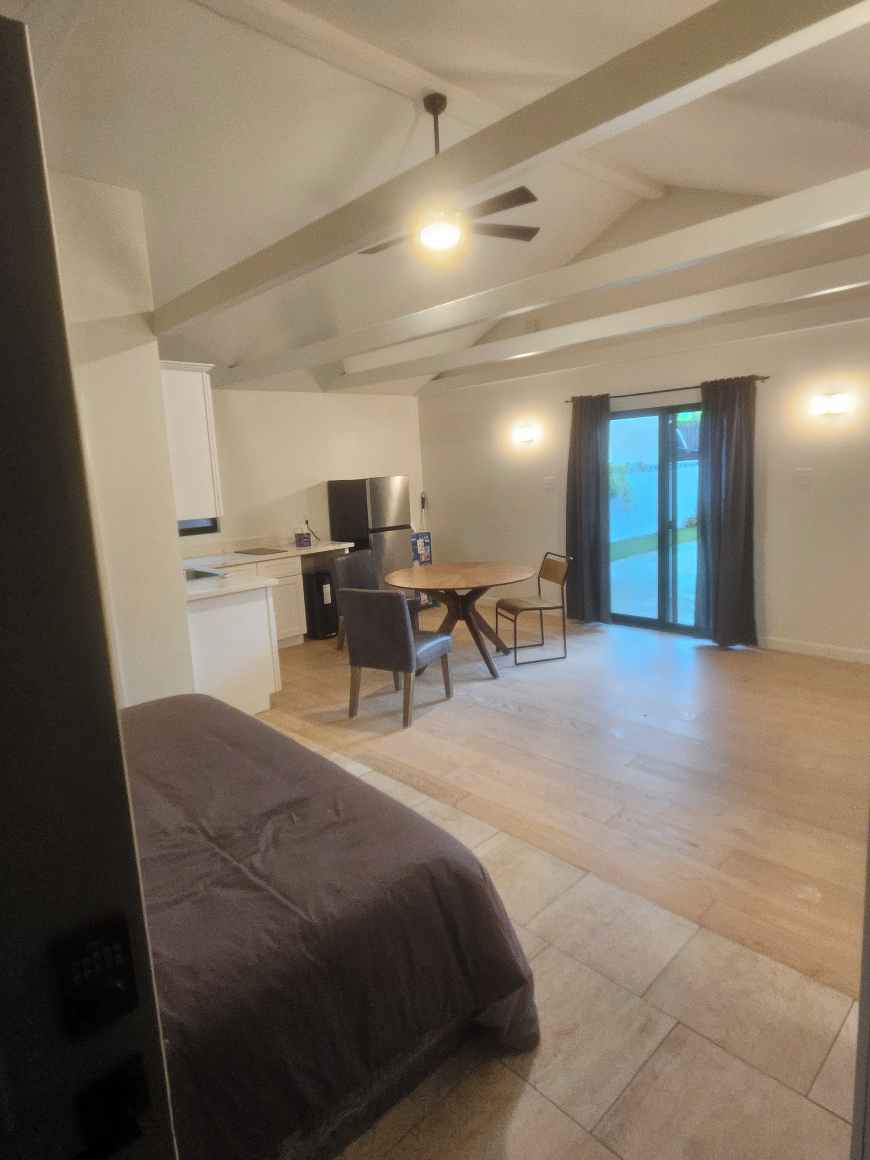 Ein Schlafzimmer mit Bett, einer Küchenzeile, einem Essbereich mit Stühlen und einem Deckenventilator.