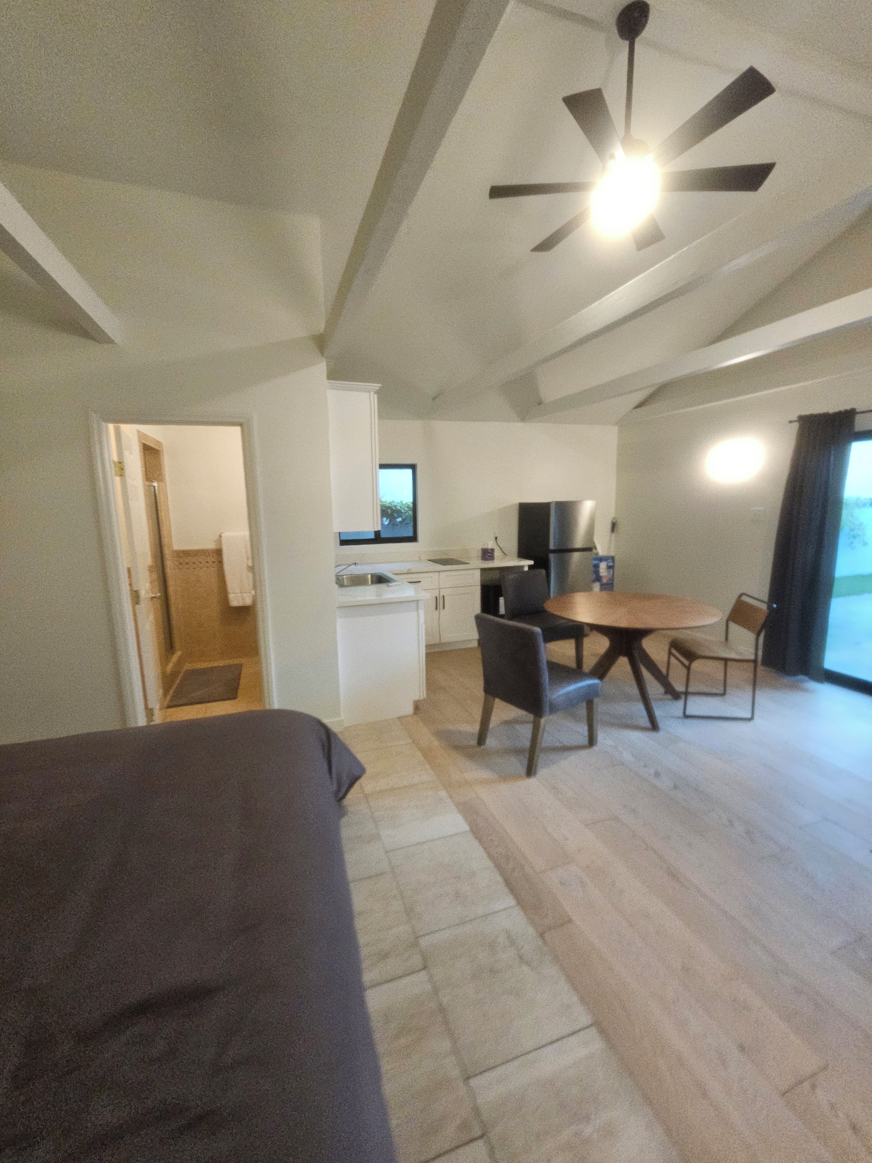 A compact room with a bed, a kitchenette, a dining area, and a ceiling fan.